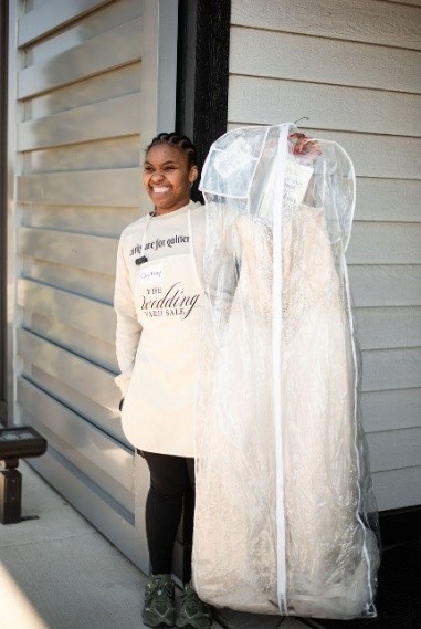 A woman smiling while holding a wedding dress in a garment bag