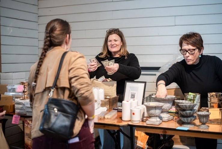 Three women at a table exchanging money and items